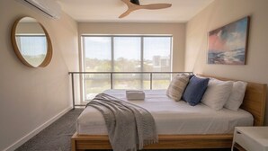 A bedroom with a bed, a window, a ceiling fan, a painting, and a round mirror. - Bright Turner Apartment with Parking and WiFi (Turner)