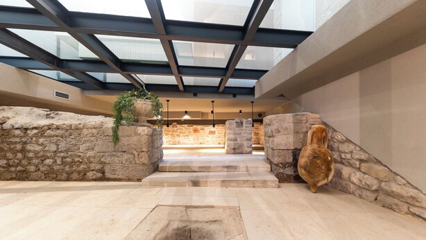 Un atrium aux murs de pierre, doté d’une verrière, d’un foyer central et d’un escalier menant à un niveau supérieur.