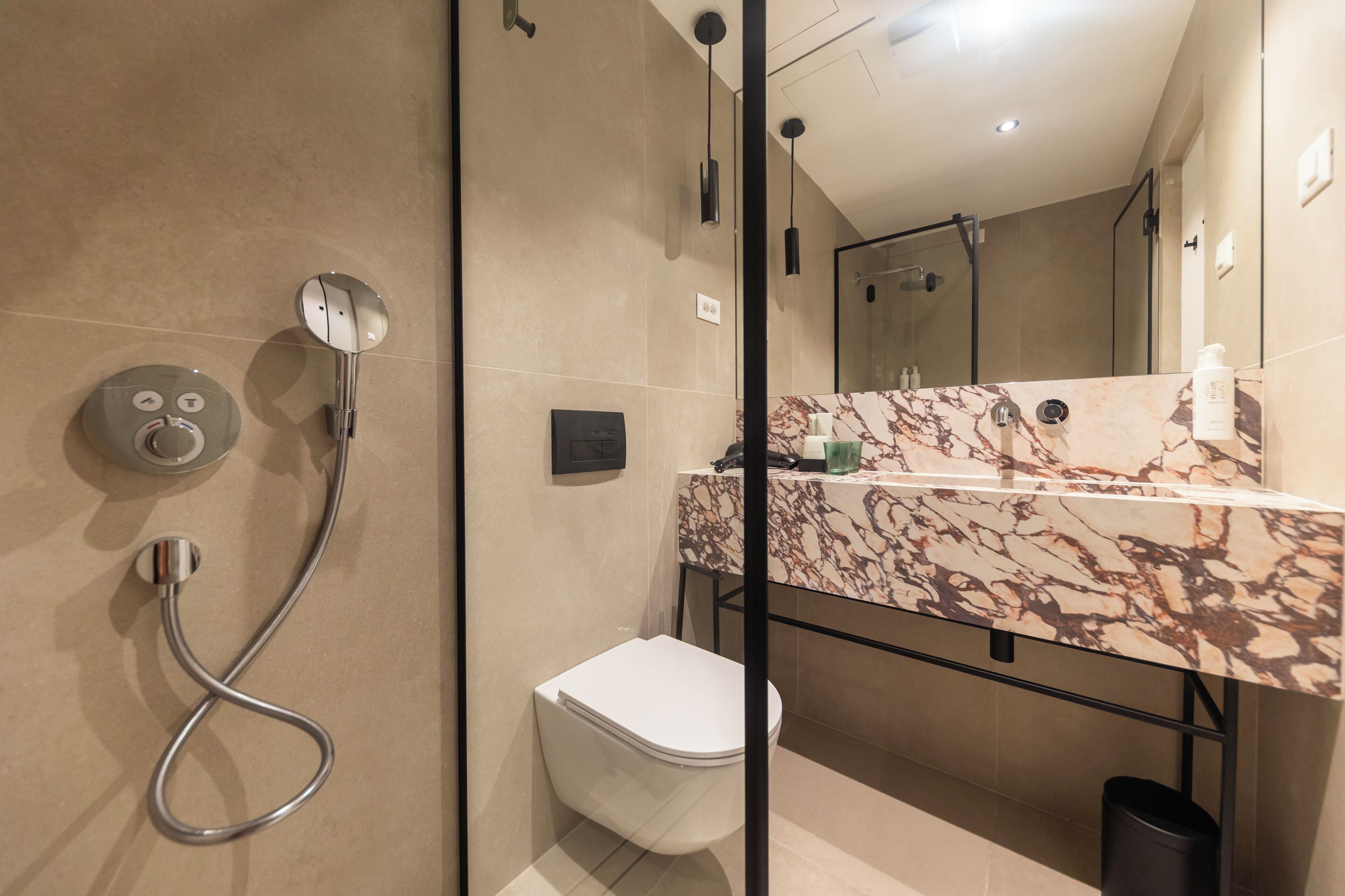 A modern bathroom with a glass shower enclosure, a marble countertop, and a toilet.
