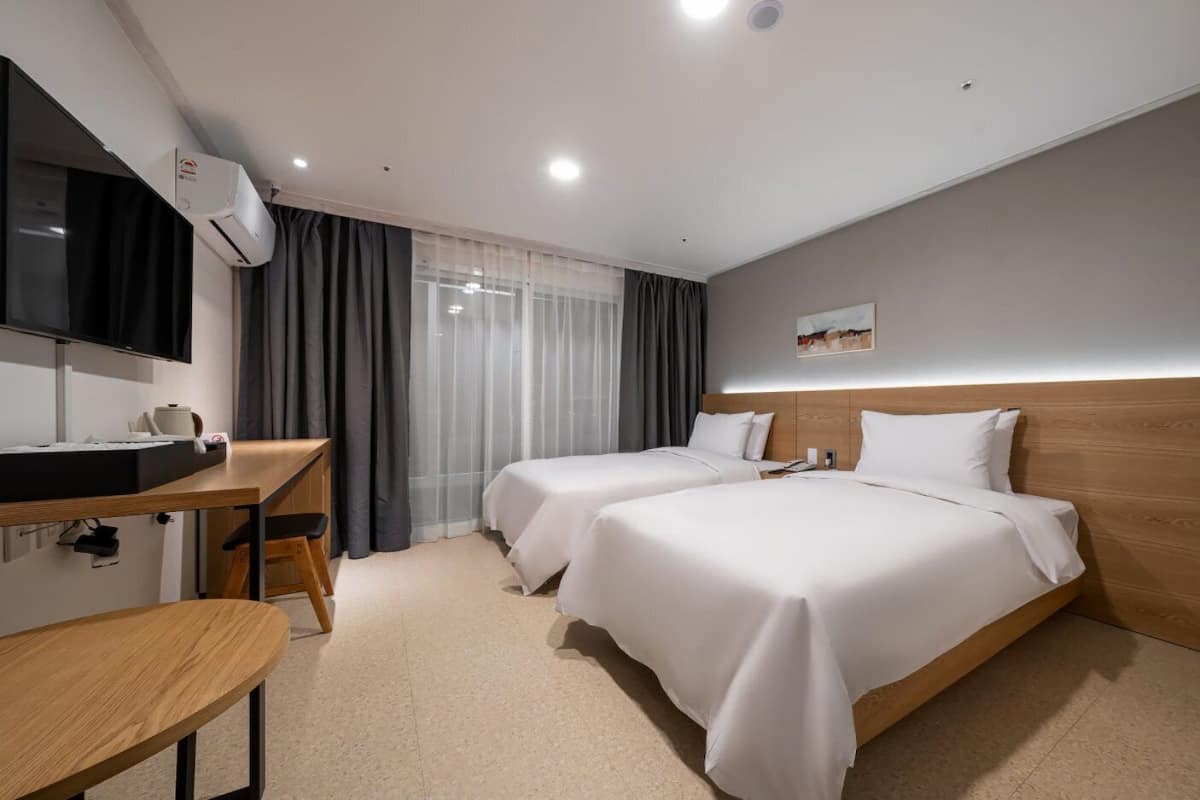 Una habitación de hotel con dos camas, un escritorio, un televisor y una ventana con cortinas.