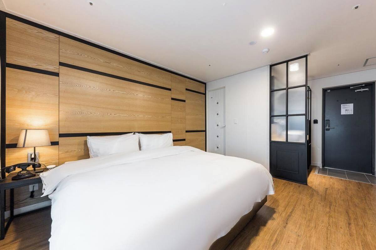 Habitación de hotel con una cama grande, un escritorio con lámpara, una silla y una puerta con paneles de vidrio esmerilado.