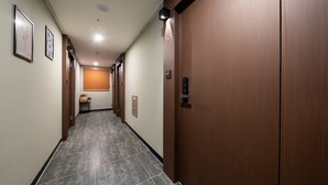 A hotel hallway with wooden doors, a tiled floor, and framed artwork on the walls.