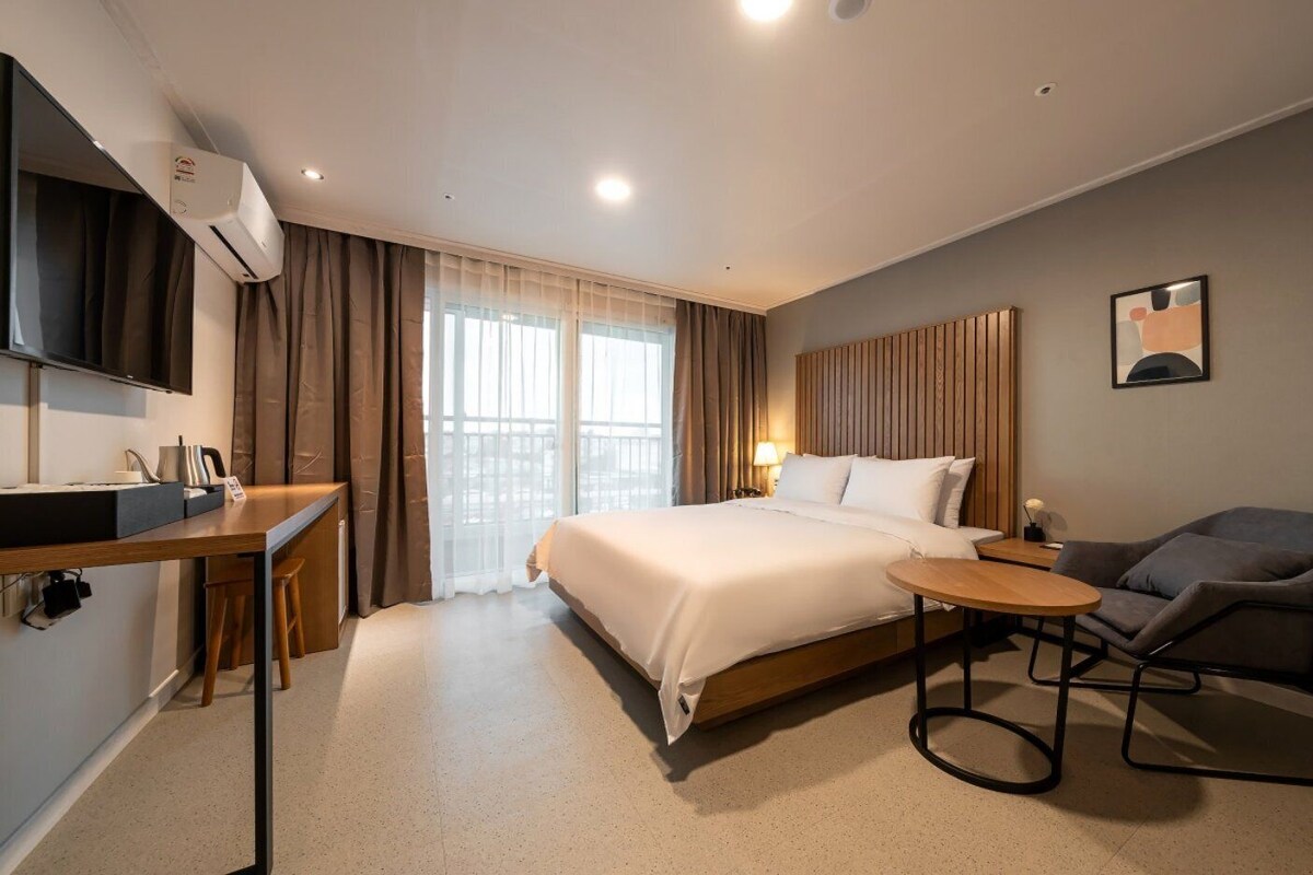 Habitación de hotel con cama, escritorio, silla y televisor montado en la pared.