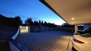 A covered parking area with a paved floor, a stone wall, and a car parked inside.