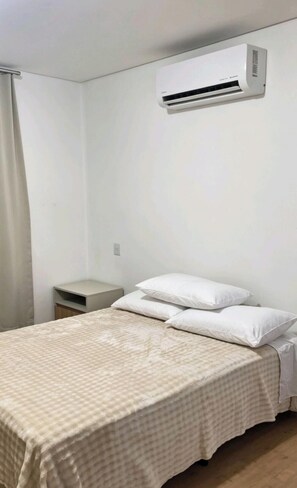 A bedroom with a bed, pillows, a nightstand, and an air conditioning unit. - Apartment with a beautiful view of the Serra Valley. (Gramado)