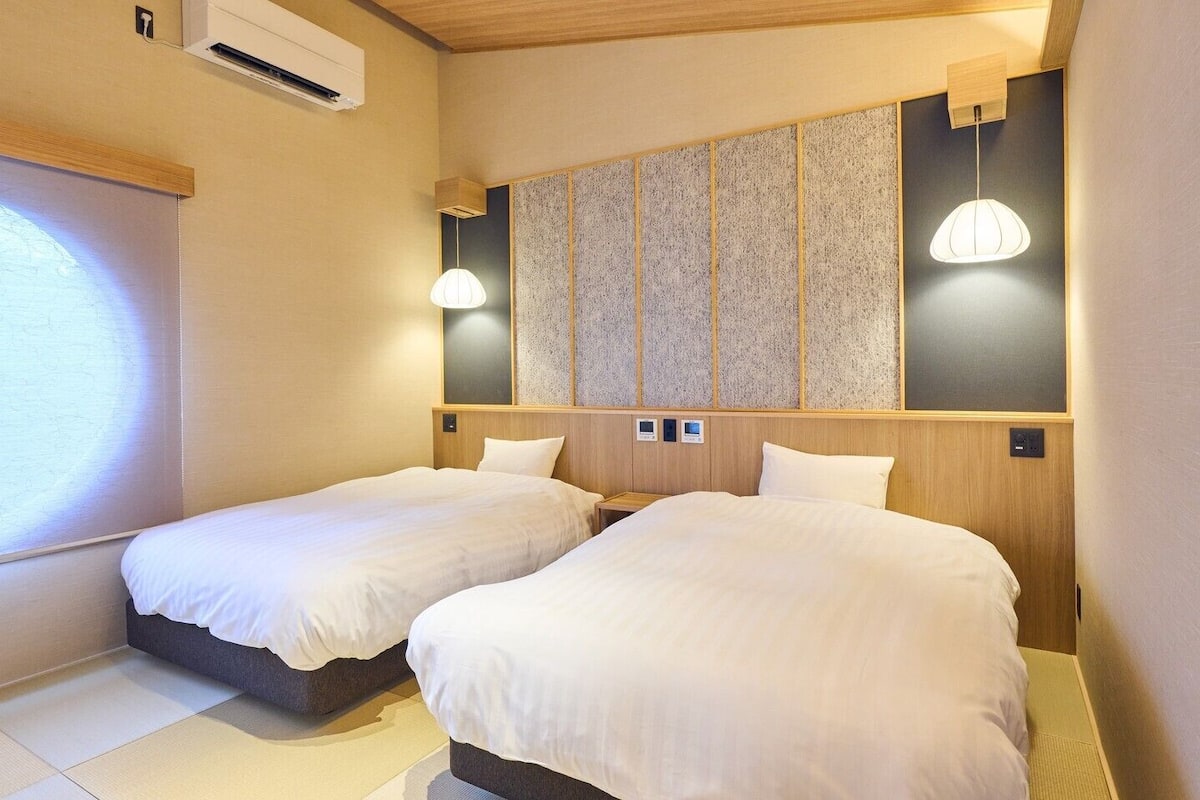Habitación de hotel con dos camas, un ventanal grande y un equipo de aire acondicionado instalado en la pared.