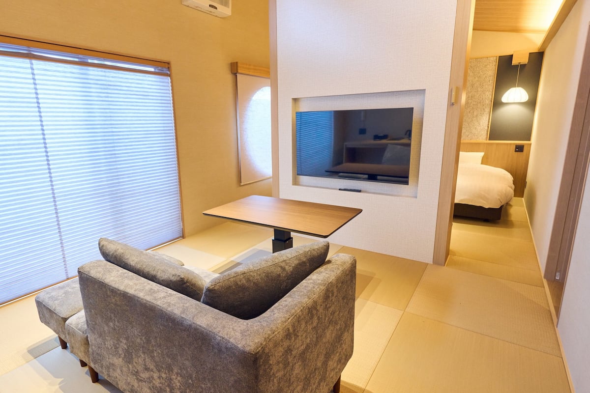 Habitación de hotel con sofá, una pequeña mesa, televisor montado en la pared y una cama con cabecera de madera.