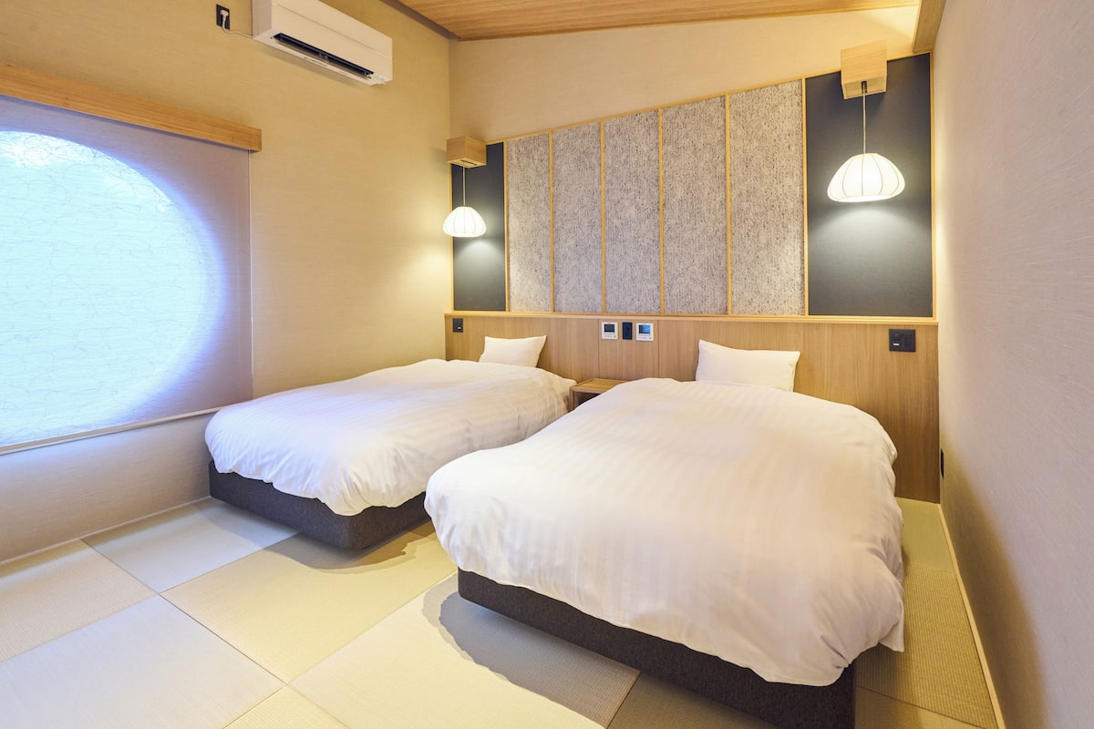 Habitación de hotel con dos camas, un ventanal grande y un panel de pared tradicional.