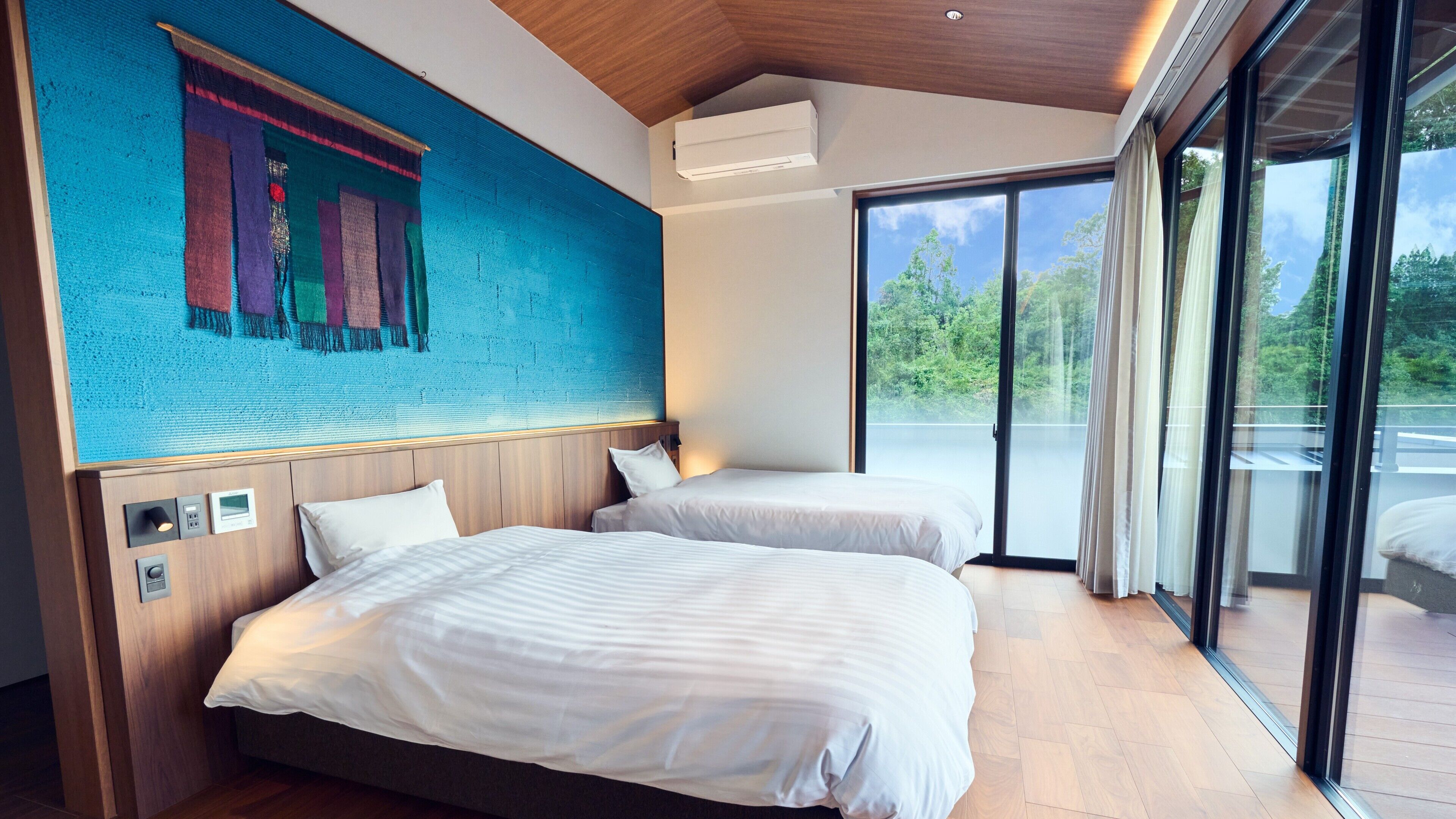 A modern hotel room with two beds, a large window, and a view of the outdoors.