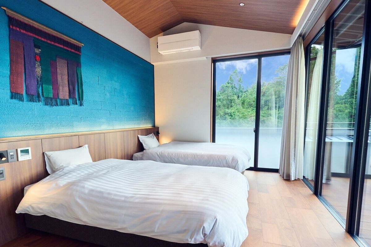 Una habitación de hotel moderna con dos camas, un ventanal grande y un mural en la pared.