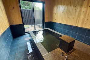 A spa area with a hot tub, wooden walls, and a view of the outside.