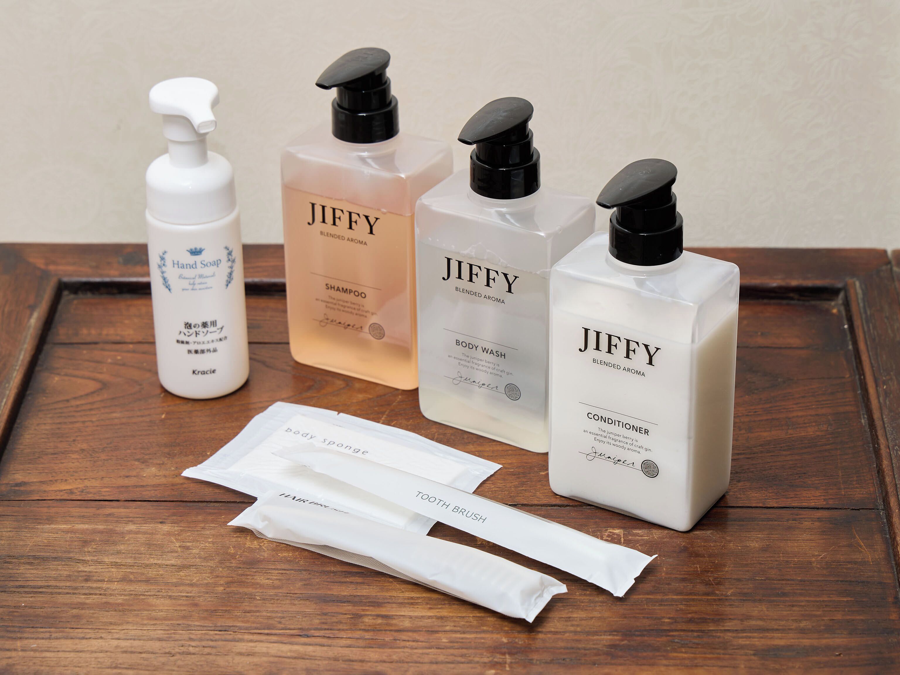 Cuatro jabones de manos Jiffy, un exfoliante corporal, un acondicionador y dos paquetes de cepillo de dientes y cabello sobre una bandeja de madera.