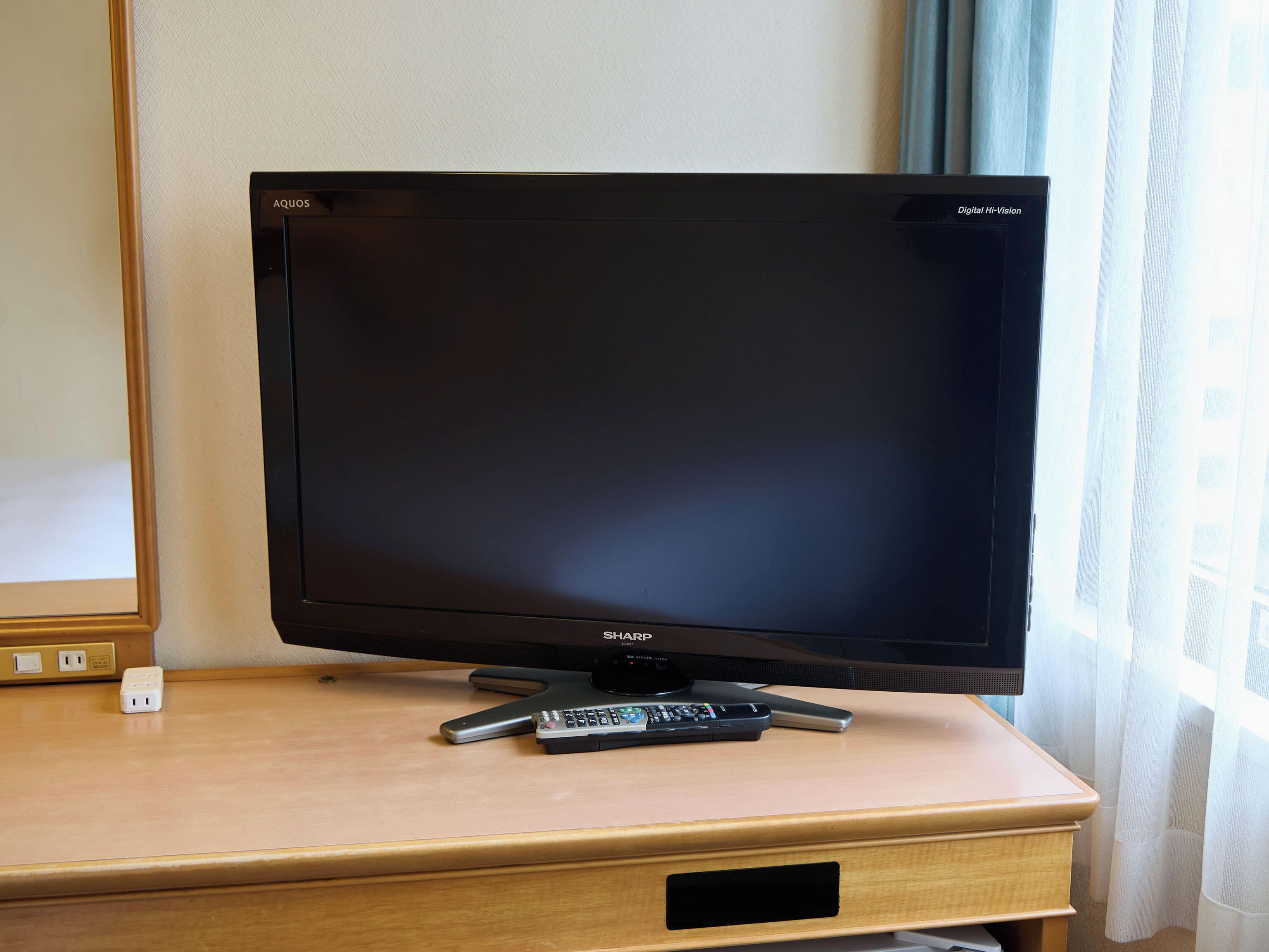 A television on a wooden desk with a remote control, a power outlet, and a cable box.