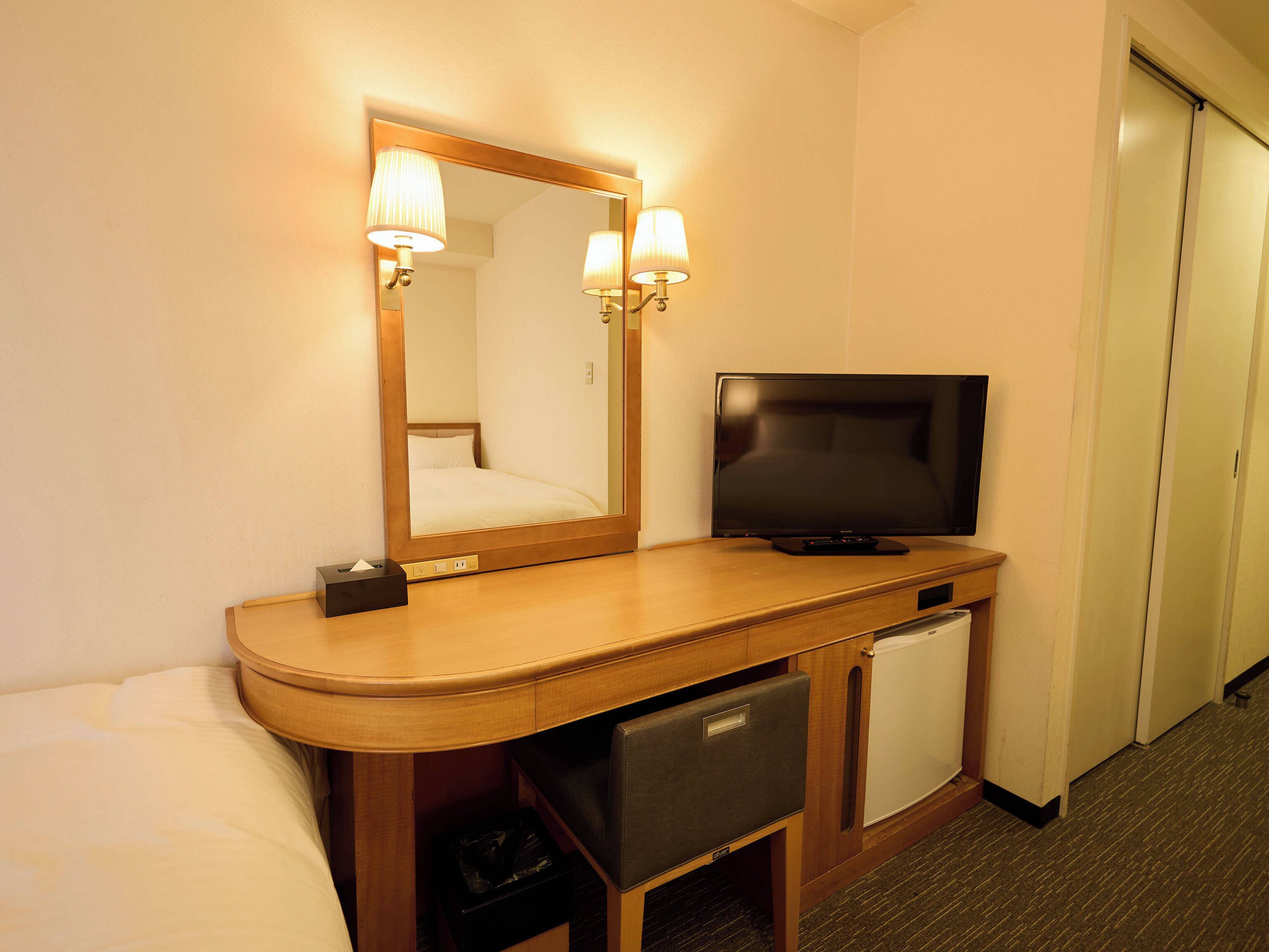 A hotel room with a bed, a television, a mirror, and a small refrigerator.