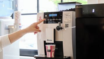 A coffee machine with a digital display, a payment button, and a cup holder for a branded cup.