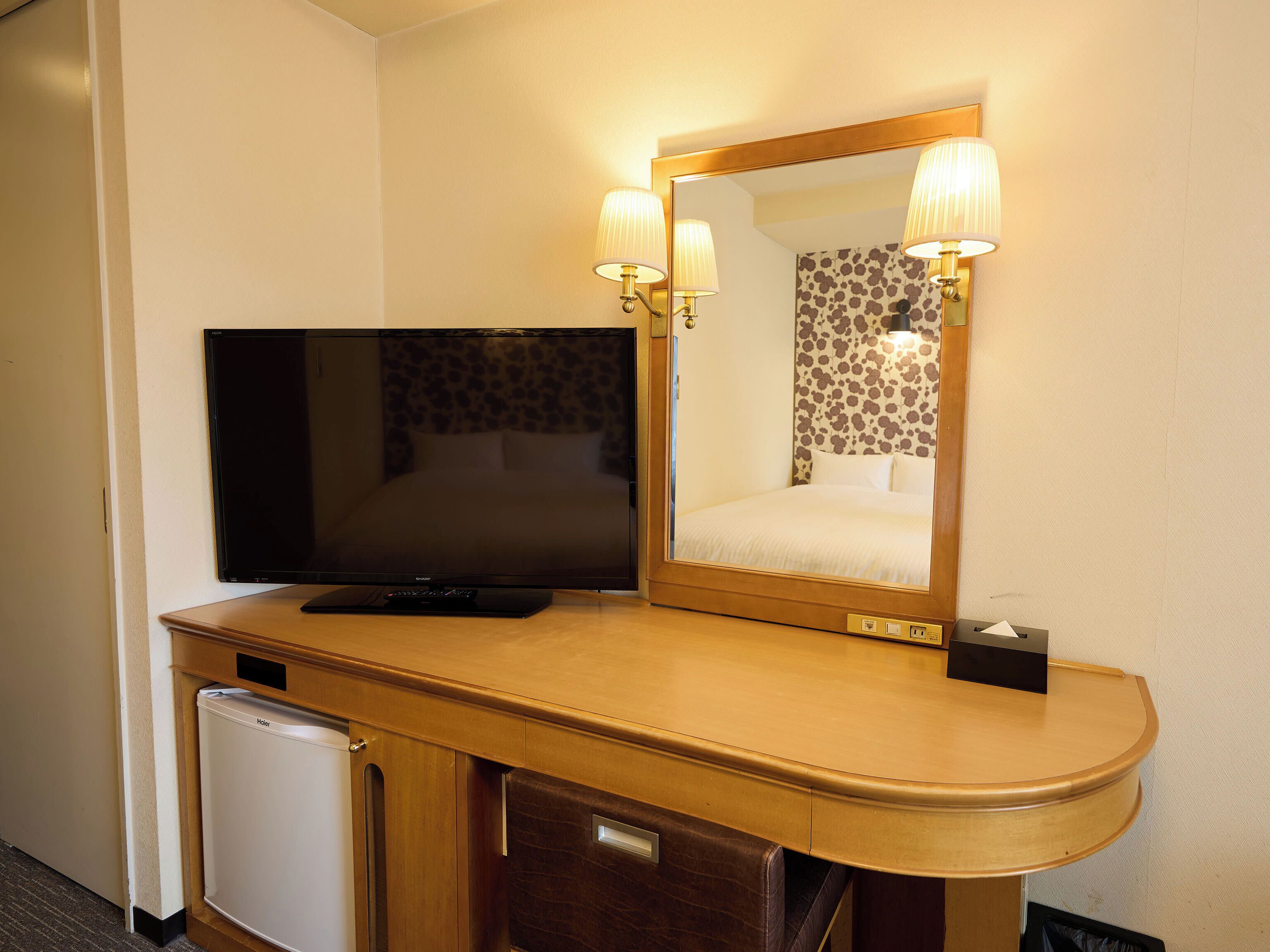 A hotel room with a television, a mirror, and a minibar.