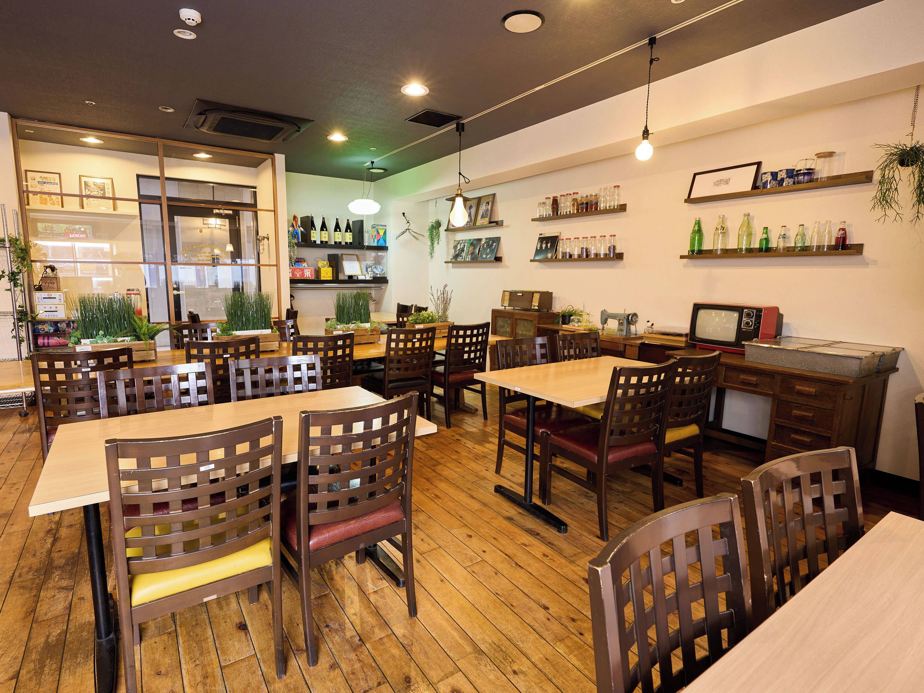 Interior de restaurante con mesas y sillas de madera, una barra con televisor antiguo y estantes con botellas.