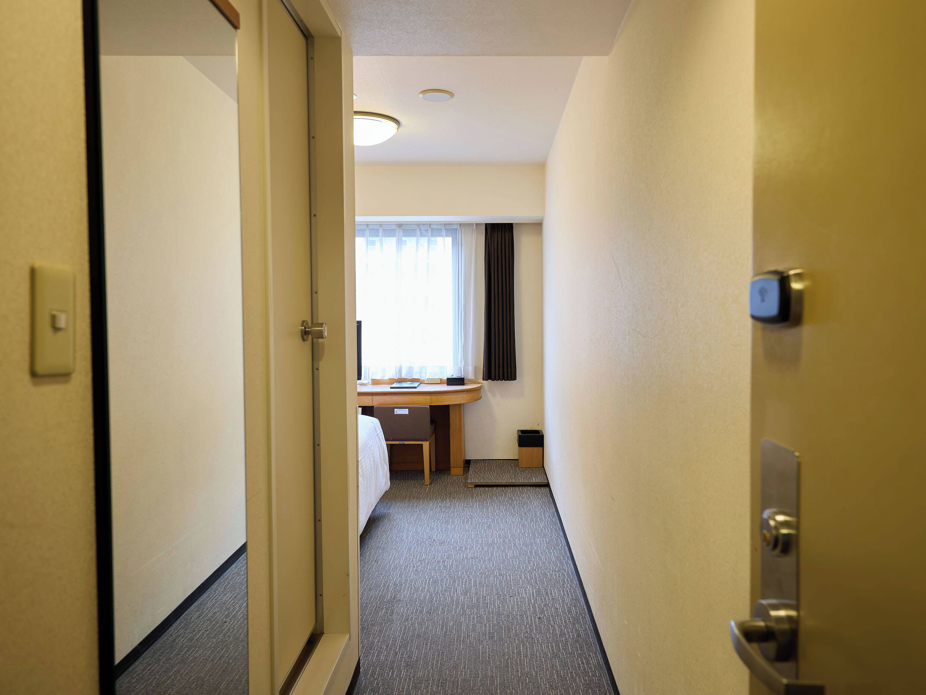 A hotel hallway with carpeted floors, a desk with a chair, a window with curtains, and a door with a lock.