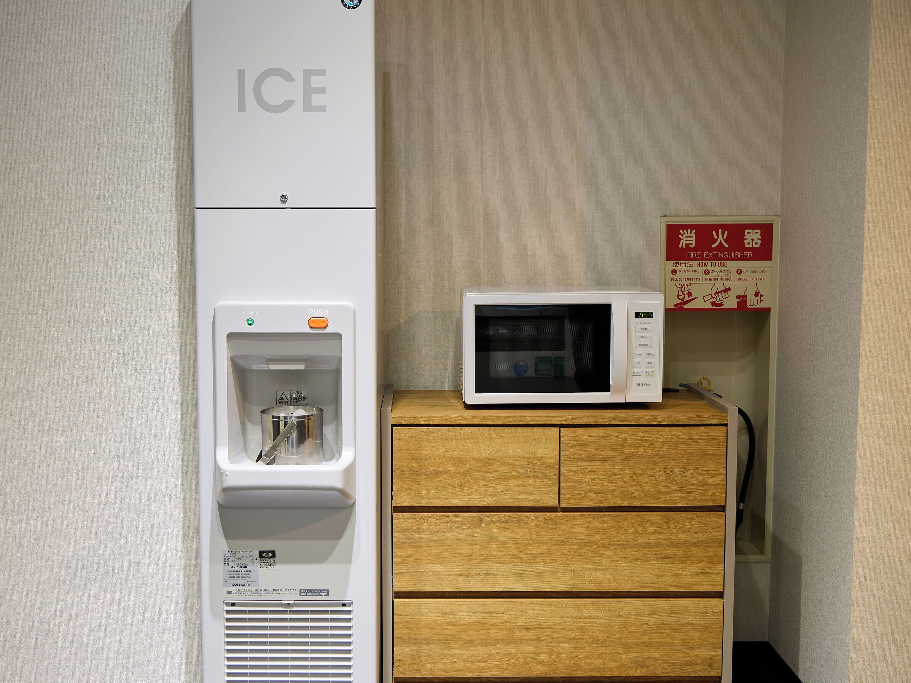 A microwave on a wooden cabinet, a water dispenser with a bottle, and a fire extinguisher on the wall.