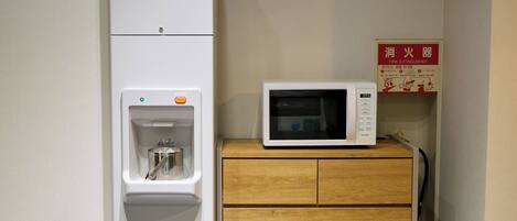 A microwave on a wooden cabinet, a water dispenser with a bottle, and a fire extinguisher on the wall.