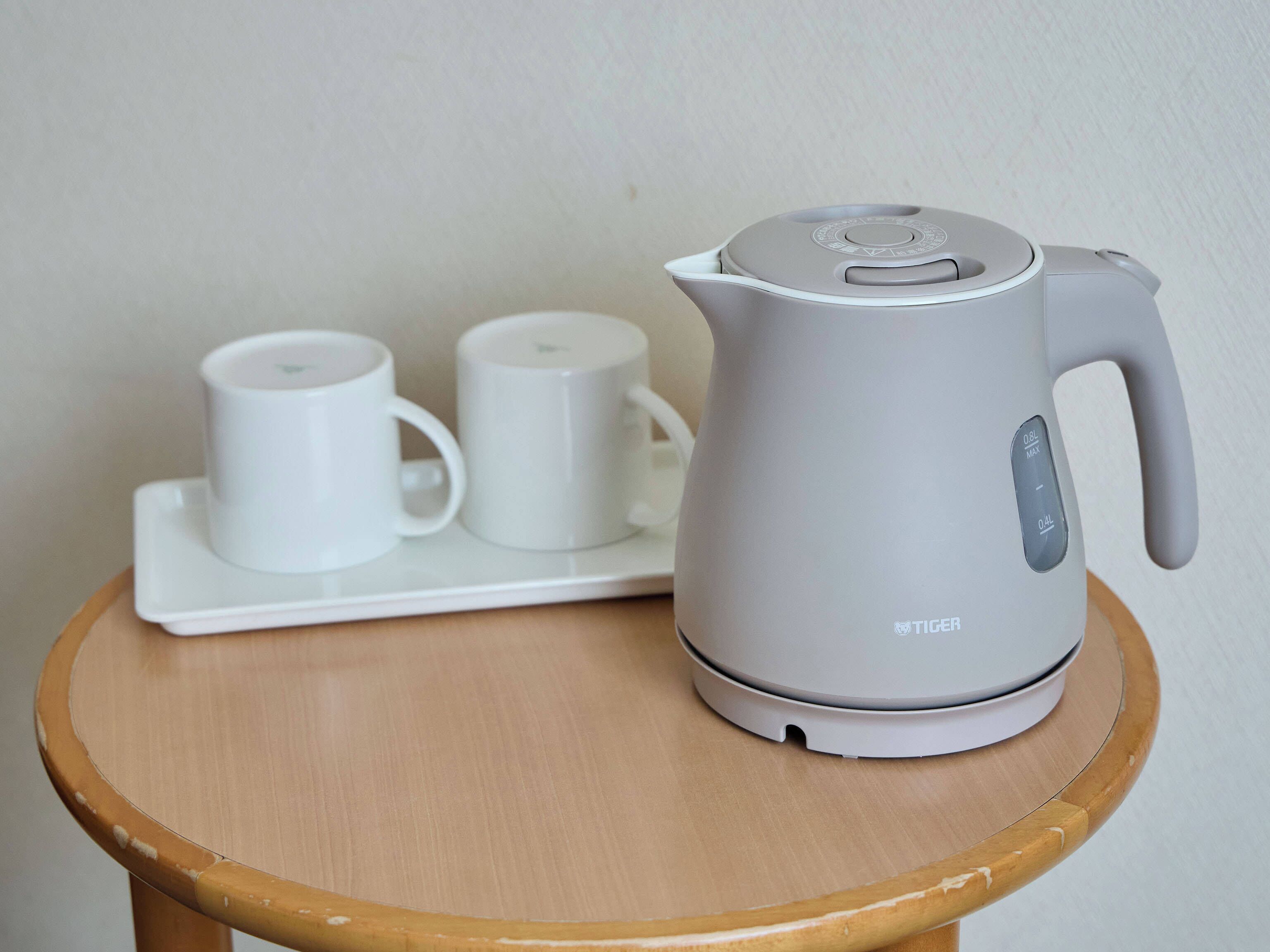 A kettle on a wooden table with a white tray holding two white cups.