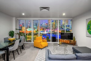 A modern living room with a city view, a dining area with a glass table, and a TV on a wooden stand. - Exclusive Stays - Southgate 28 (Southbank)