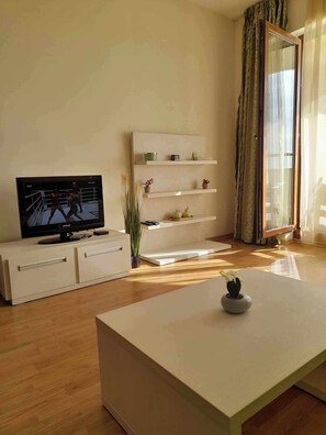 Un salon moderne doté d’un téléviseur à écran plat, d’une console blanche, d’une table basse et d’une étagère au design minimaliste.