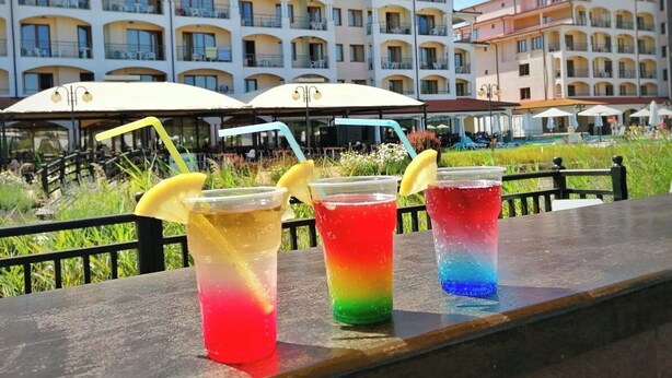 A row of colorful drinks on a table with a hotel building in the background. - Apartment mit 2 Schlafzimmern in Obzor - 6 Pools & Bio- See (Obzor)