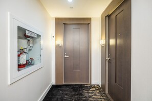 Un couloir avec un extincteur fixé au mur, une porte et un tapis à motifs noirs et jaunes.