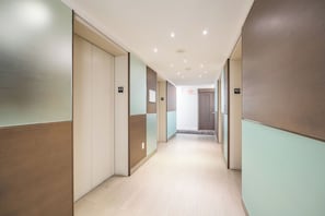 Un couloir avec des portes numérotées de 43, un sol de couleur claire et un plafond sobre agrémenté d’un éclairage encastré.