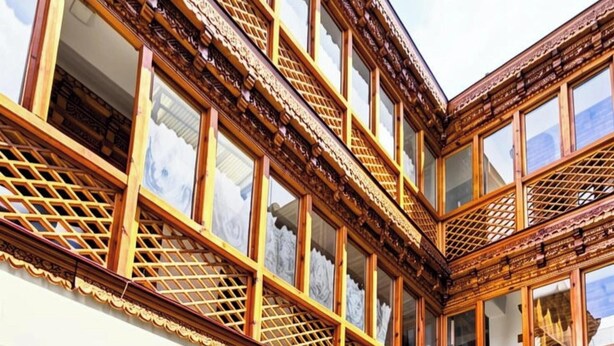 Um edifício tradicional com varandas de madeira, várias janelas e área externa com móveis de vime.