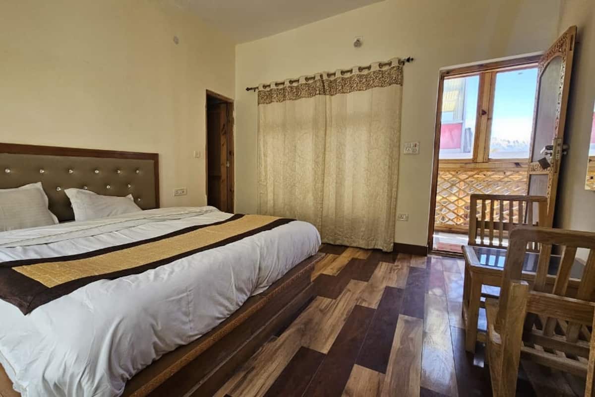 A bedroom with a bed, wooden floor, curtains, and a view through a window.