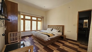 Quarto com cama, piso de madeira, escrivaninha e janela com cortinas.