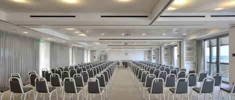 A conference room with rows of chairs, a projector screen, and large windows.