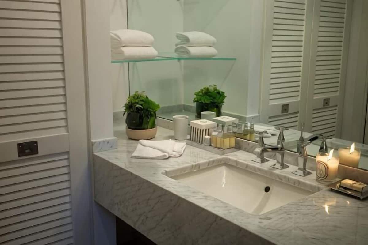 Un baño con lavamanos de mármol, estantes de vidrio, una planta en maceta y artículos de aseo.
