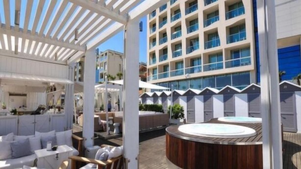 Una terraza en la azotea con mobiliario exterior, un jacuzzi y un edificio moderno al fondo.