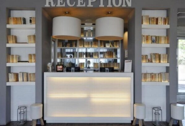 A reception area with a counter, two large lamps, and bookshelves on either side. - Excelsior Hotel, Spa & Lido (Pesaro)