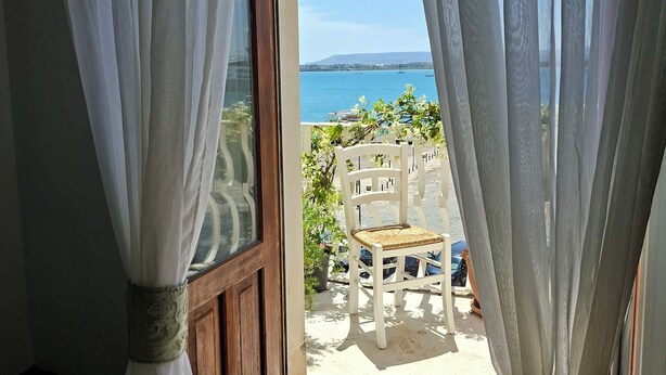 Habitación con vista al mar, cortinas de lino traslúcidas, una puerta de madera y una silla blanca en el exterior.