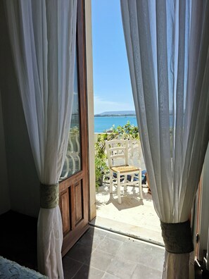 A room with a view of the sea through sheer curtains, a wooden door, and a white chair outside. - La casa dei fiori sul mare (Syracuse)