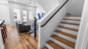 A modern interior with a staircase, wooden flooring, a grey sofa, and a dining area. - Private Gated Townhome Near Med Center & NRG (Houston)