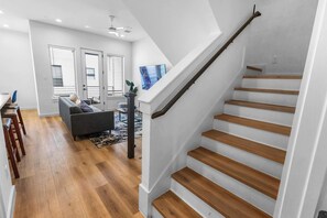 Een modern interieur met een trap, houten vloeren, een grijze bank en een eethoek.
