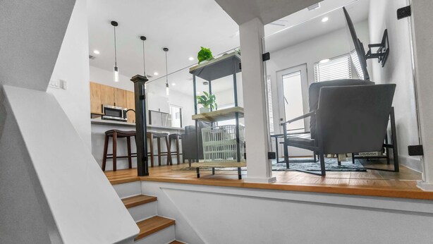 A modern interior with a staircase leading to a living area, a kitchen, and a dining space. - Private Gated Townhome Near Med Center & NRG (Houston)