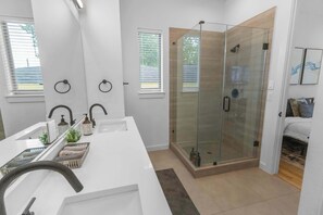 Een moderne badkamer met een douchecabine van glas, een witte wastafel met een gebogen kraan en een kleine plant op het aanrecht.