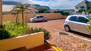A residential area with a paved driveway, parked cars, and a view of distant mountains. - Outspan Lodge- Giraffe House (Cape Town)