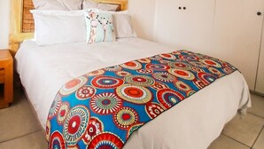 A bedroom with a bed, pillows, a headboard, a wall hanging, and a wardrobe. - Outspan Lodge- Giraffe House (Cape Town)