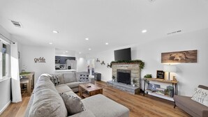 Una sala moderna con un sofá seccional gris, una chimenea y una cocina al fondo.