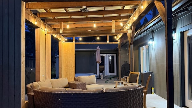 Un área de estar al aire libre techada con jacuzzi, pérgola de madera y luces colgantes.