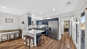Una cocina moderna con una isla central, taburetes de madera y un refrigerador de acero inoxidable.