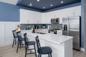 A modern kitchen with white cabinets, a stainless steel refrigerator, a microwave, and a large island with bar stools.