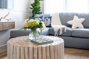 A living room with a grey sofa, a round wooden coffee table with a vase of flowers, and a blue cushion.
